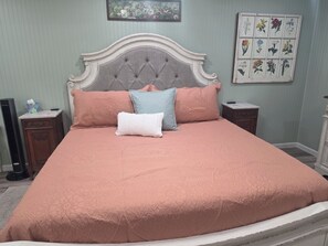 A bed with a tufted headboard, multiple pillows, and a floral wall art piece.