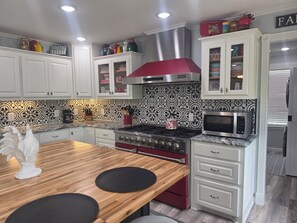 A modern kitchen with white cabinets, a red stove, a microwave, and a patterned backsplash.