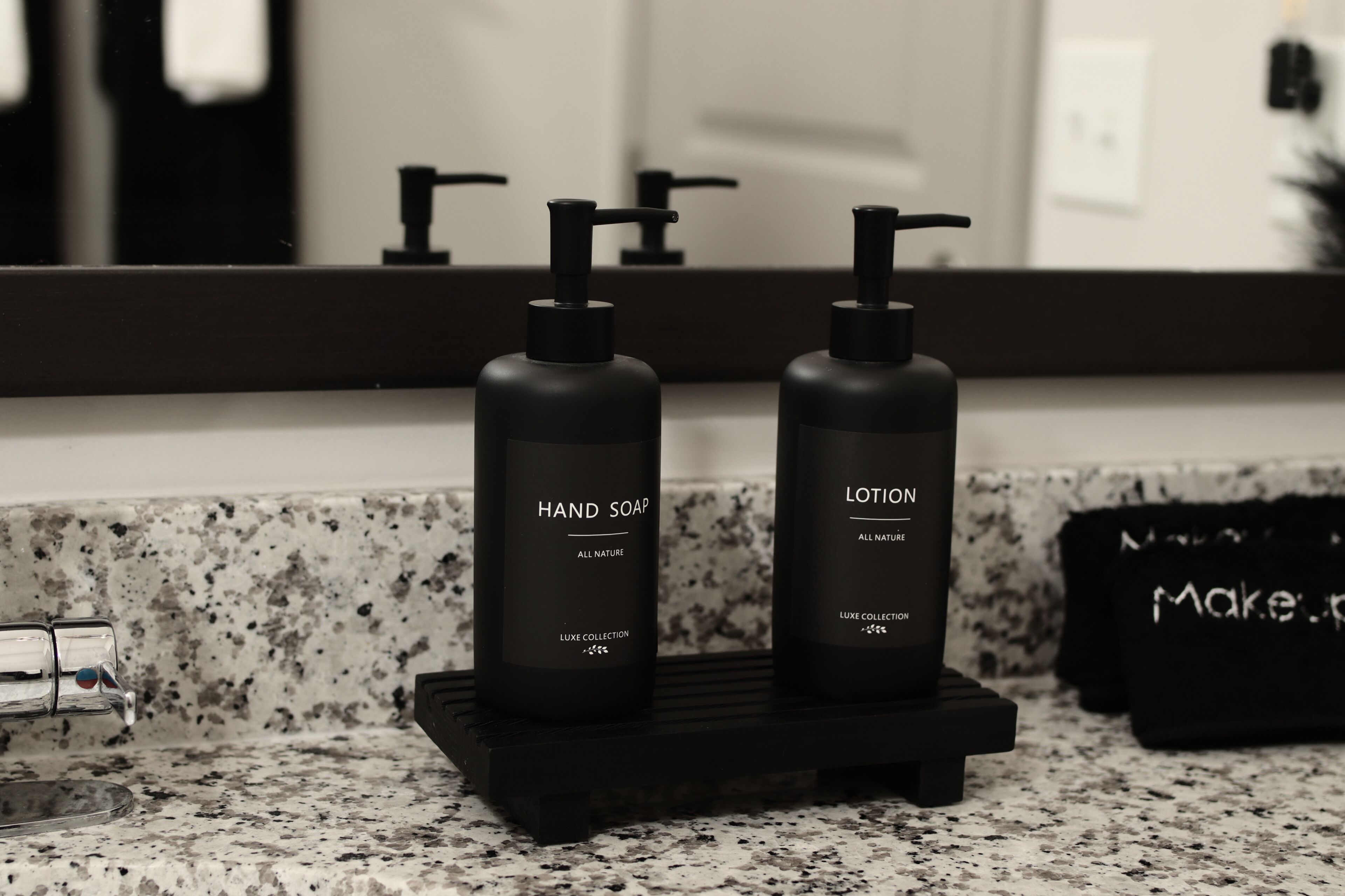 A bathroom vanity with two black bottles labeled 'HAND SOAP' and 'LOTION' on a black tray.