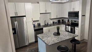 Una cocina moderna con armarios blancos, electrodomésticos de acero inoxidable, encimeras de granito y un taburete de bar.