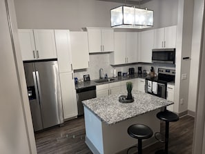 Una cocina moderna con armarios blancos, electrodomésticos de acero inoxidable, encimeras de granito y un taburete de bar.