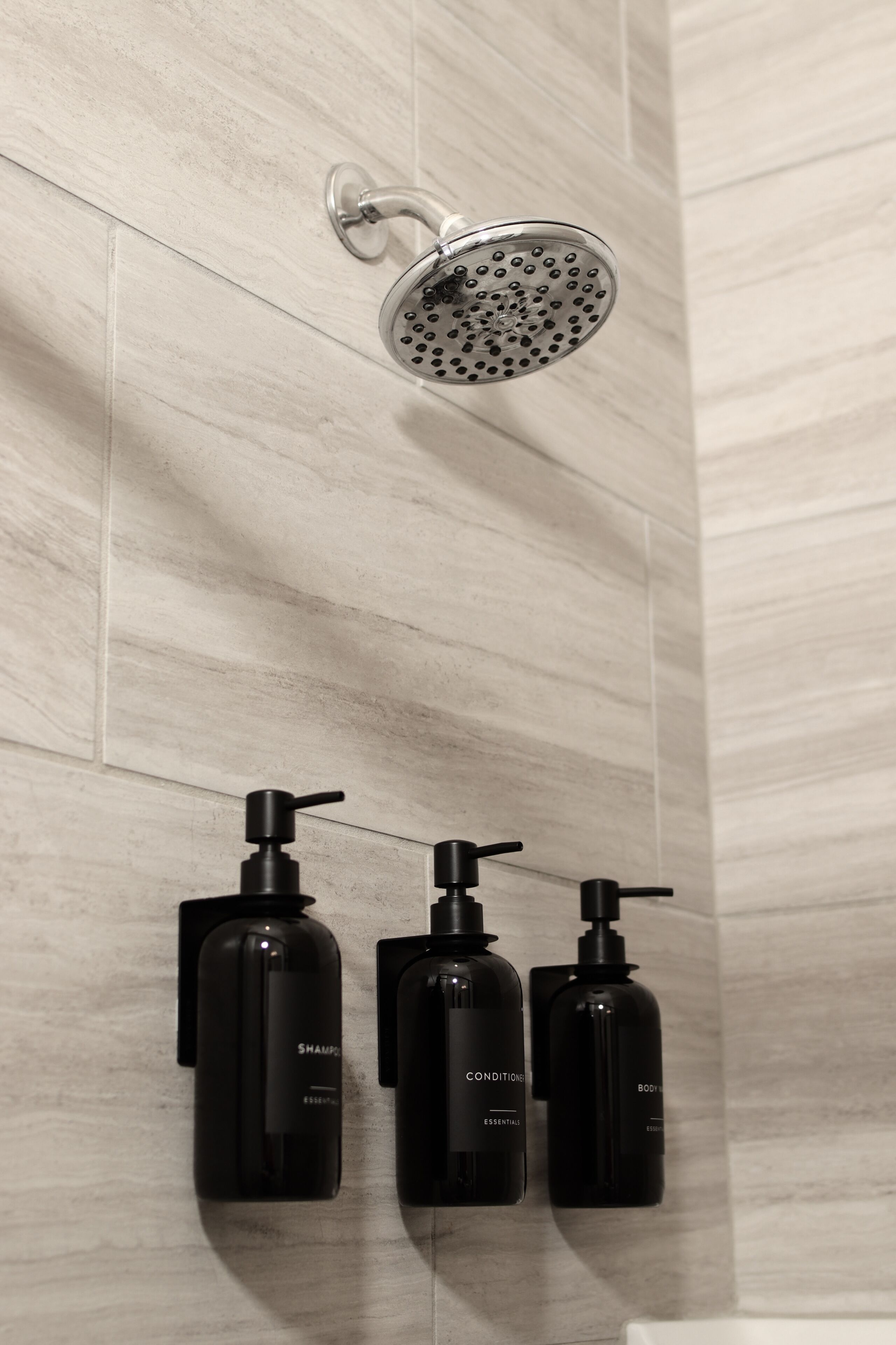 Un cabezal de ducha, tres botellas negras de champú, acondicionador y gel de baño, y una bañera blanca.