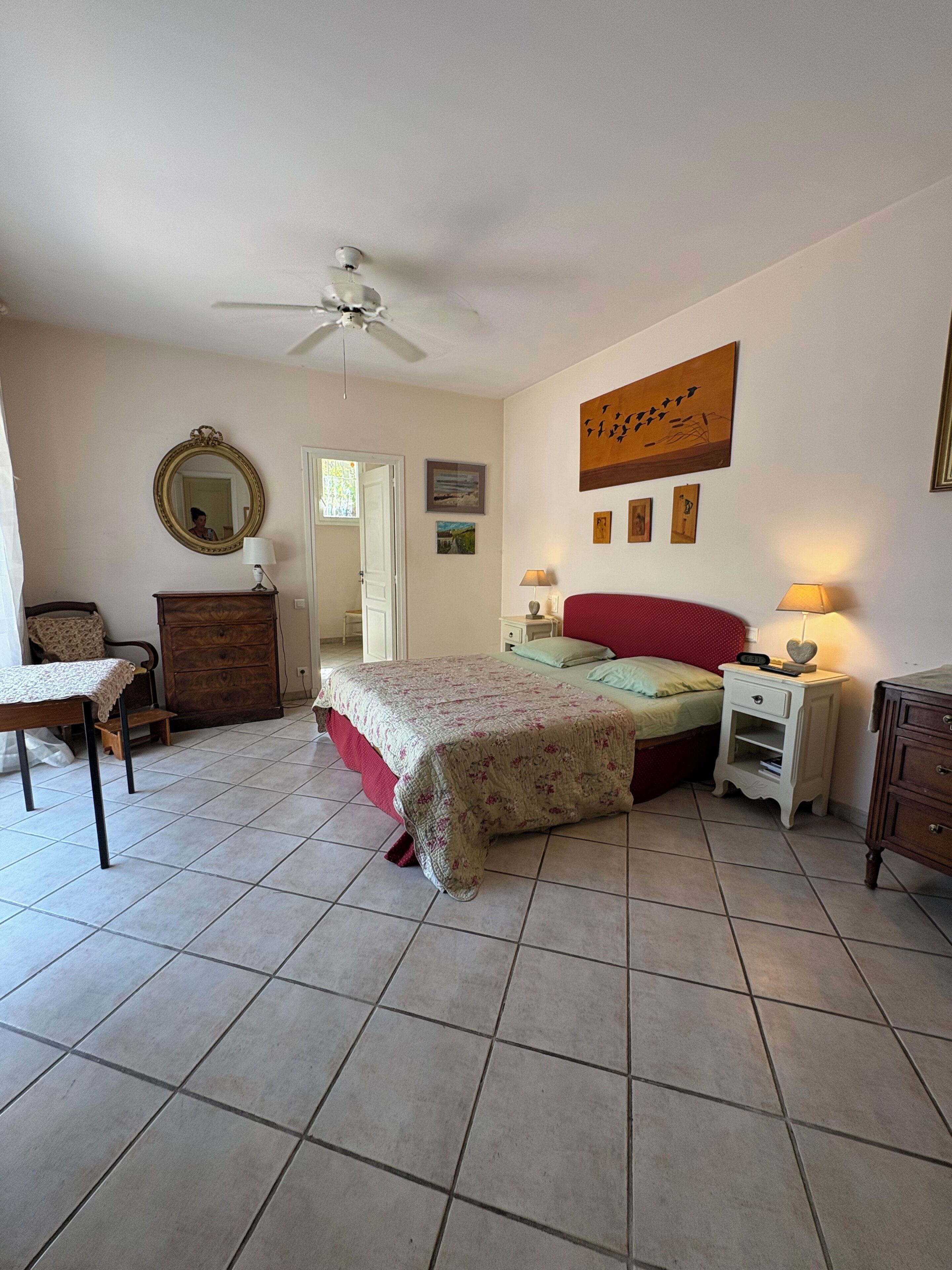 Ein Schlafzimmer mit Bett, Kommode, Nachttisch, Stuhl, Spiegel und Deckenventilator.