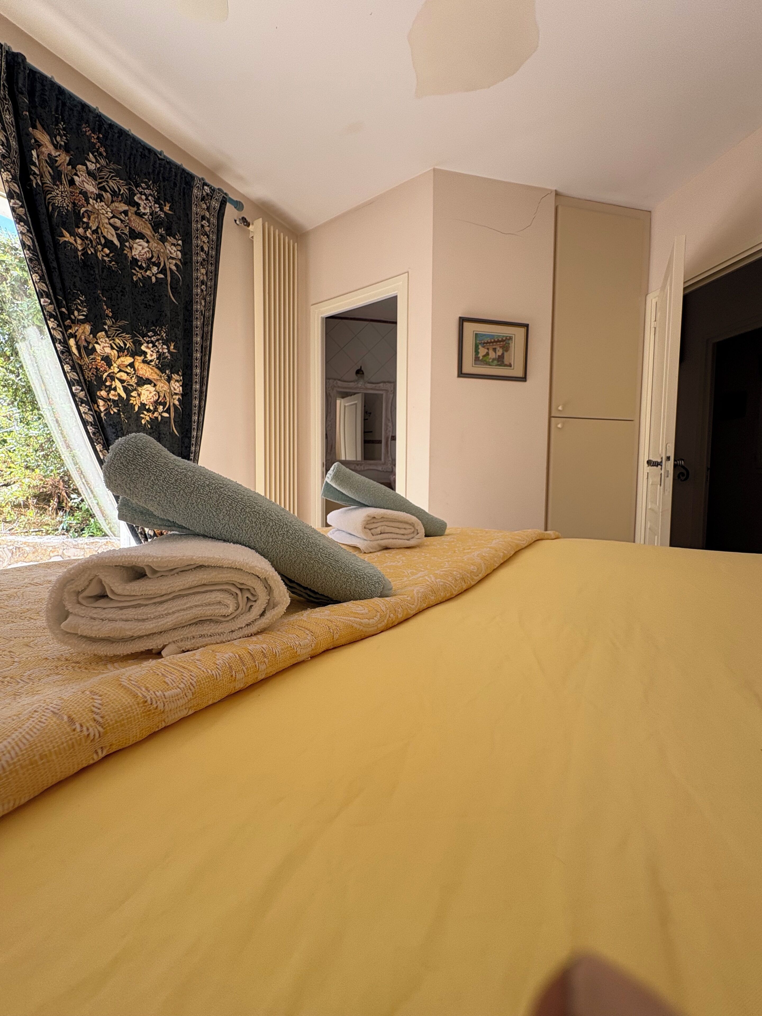 Ein Hotelzimmer mit Bett, einem Fenster mit Vorhängen, einer Tür und einem gerahmten Bild an der Wand.
