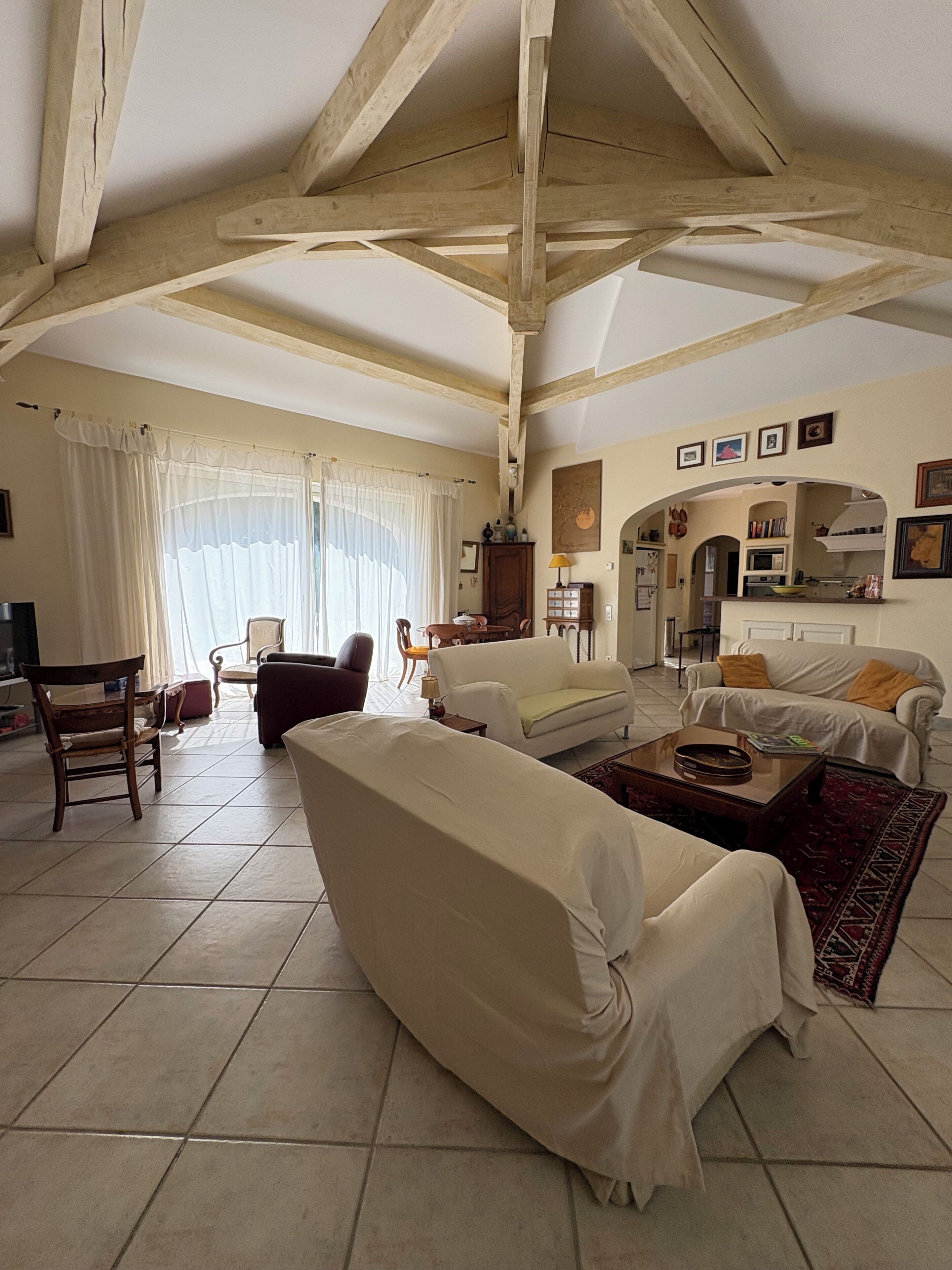 A spacious living room with a high ceiling, tiled floor, and a fireplace. There are two sofas, a coffee table, and a dining area with chairs.