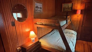 Une chambre avec un lit superposé, des murs en bois, un miroir rond, une petite table avec une lampe et deux tableaux encadrés.