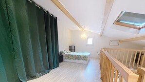 A room with a bed, a window, a ceiling light, and a wooden railing.