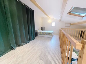 A room with a bed, a window, a ceiling light, and a wooden railing.