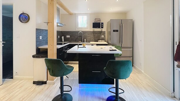 A modern kitchen with a central island, two bar stools, a microwave, and a refrigerator.
