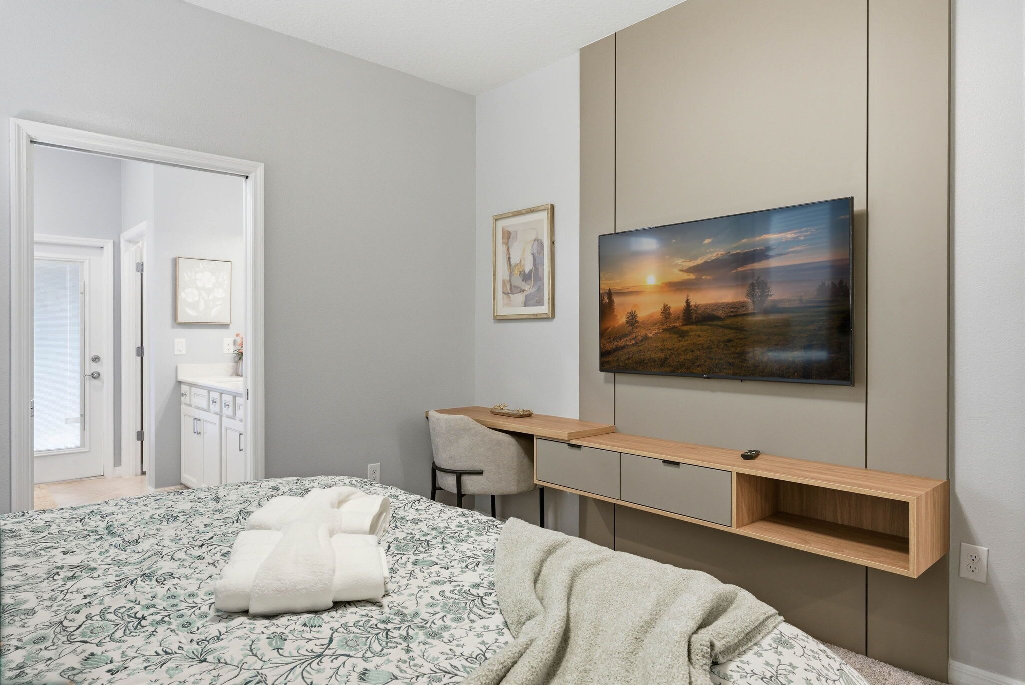 A bedroom with a bed, a desk, a chair, a TV, and artwork on the wall.