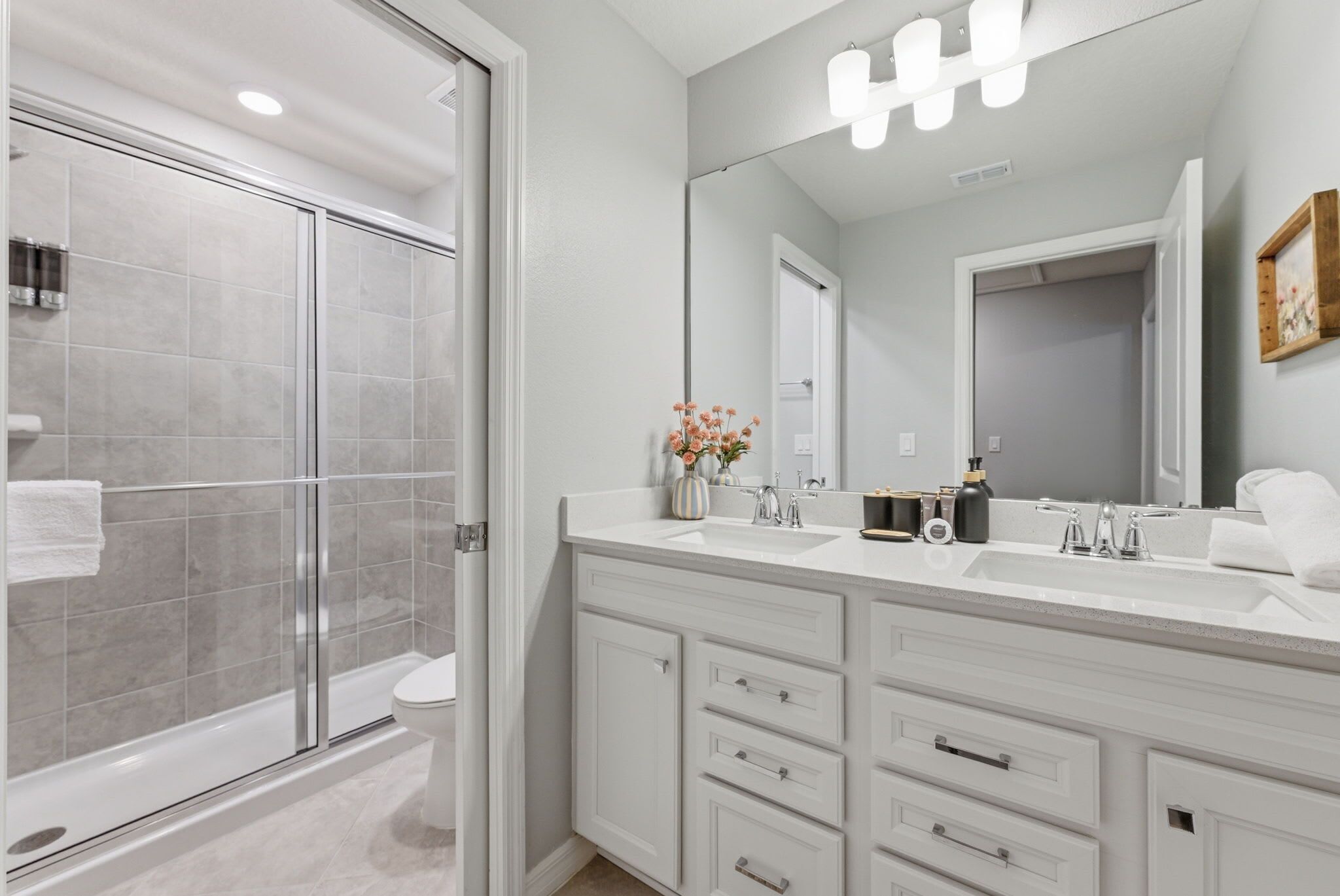 A bathroom with a glass shower enclosure, a white sink with a mirror, and a vanity with drawers.