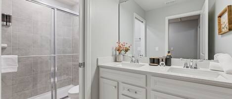 A bathroom with a glass shower enclosure, a white sink with a mirror, and a vanity with drawers.