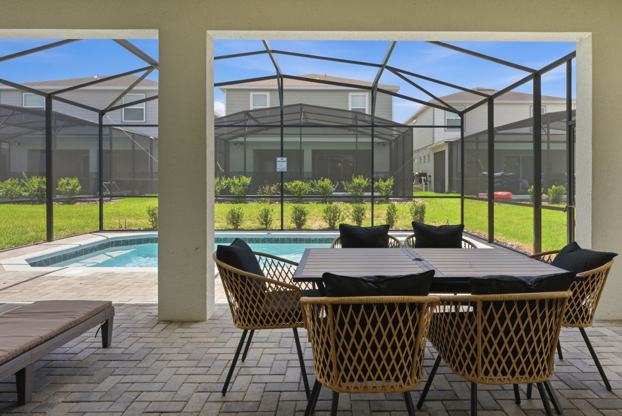 A covered patio area with a pool, outdoor furniture, and a view of a house.