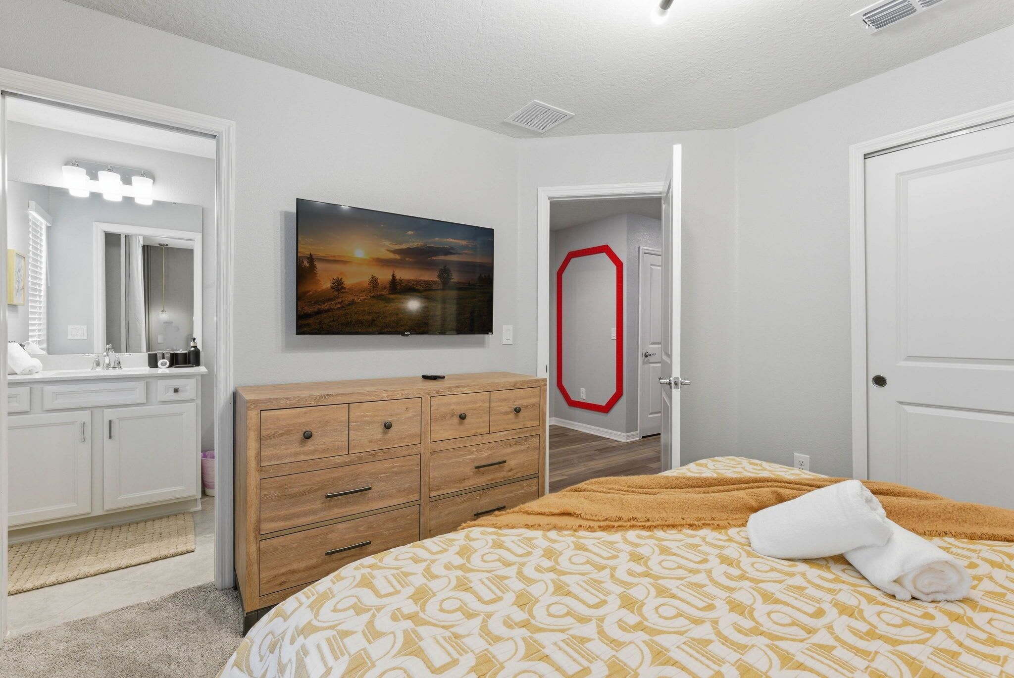Een slaapkamer met een bed, dressoir, spiegel en een schilderij aan de muur.