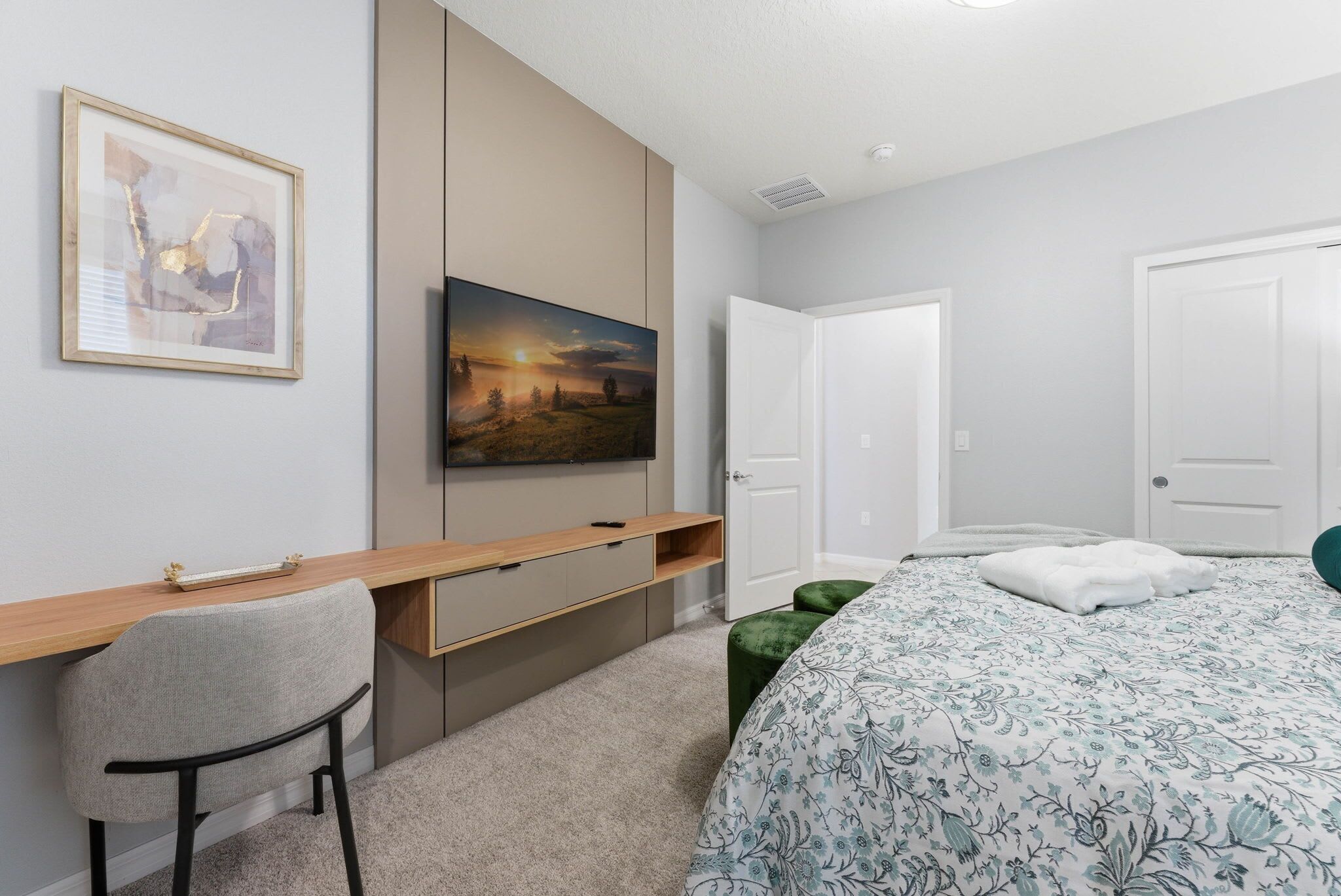 A bedroom with a bed, a desk, a chair, a television, and a door.