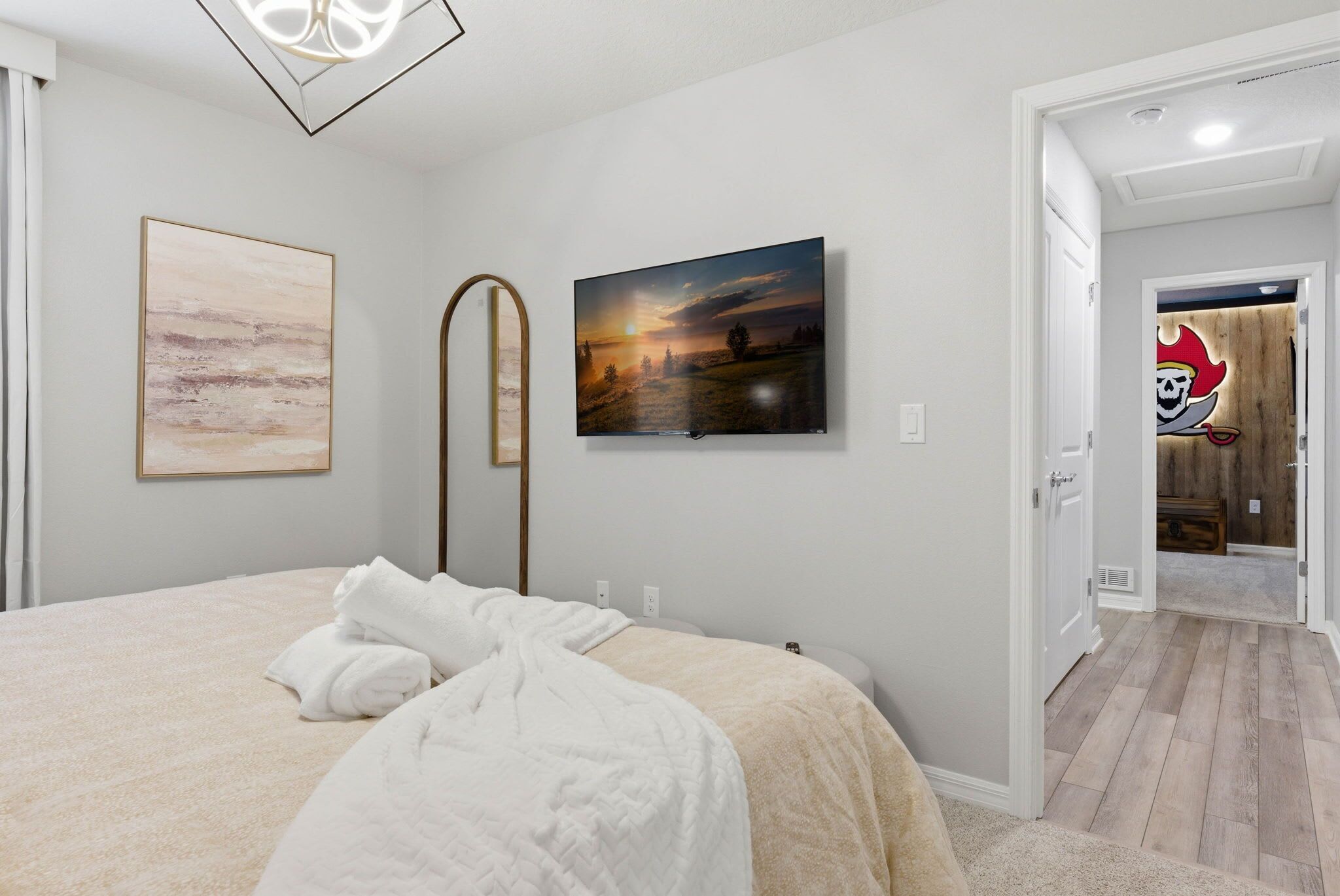 A bedroom with a bed, a painting, and a door leading to another room.