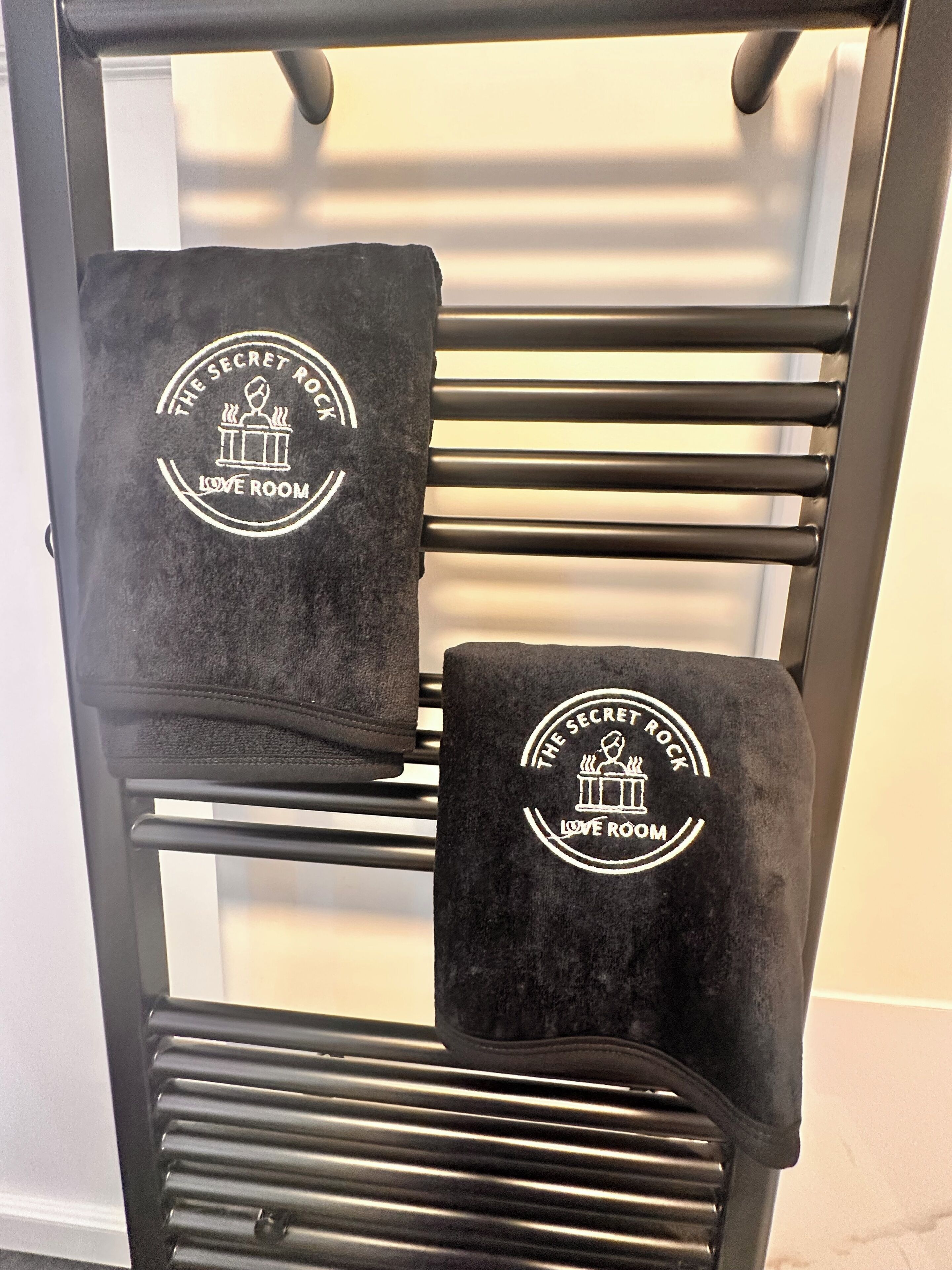 Ein Handtuchhalter mit zwei schwarzen Handtüchern, jedes mit einem Logo und Text.