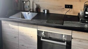 A kitchen with wooden cabinets, a stainless steel sink, a built-in oven, and a black countertop. - The Secret Rock (La Roche-en-Ardenne)