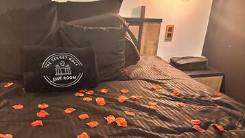 A bed with rose petals, a pillow with a logo, and a wall-mounted light fixture.