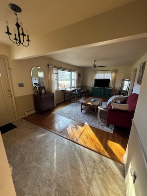 A spacious living room with a large window, a chandelier, a television, and a red sofa. - Spacious 4-bedroom house with AC in wonderful Williamsport (Williamsport)