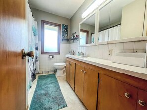 A bathroom with a toilet, sink, mirror, and a window.