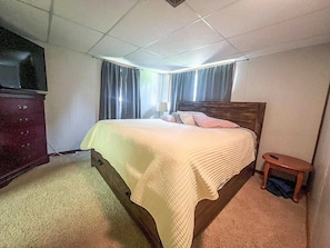 Quarto com cama, mesa de cabeceira, cômoda e televisão.