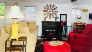 A living room with a sofa, a red armchair, a lamp, a fireplace, and a decorative wall piece. -  ROOMY SUNSHINE CABIN IN THE COUNTRY (Claremore)