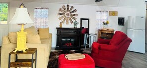 Una sala de estar con un sofá, un sillón rojo, una lámpara, una chimenea y un adorno en la pared.