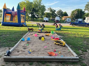A sandbox with toys and a play structure in the background. -  ROOMY SUNSHINE CABIN IN THE COUNTRY (Claremore)