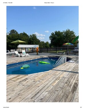 Una terraza de madera con piscina, sillas de descanso y un área techada con sombrillas.