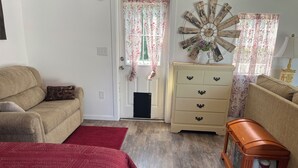 A room with a beige sofa, a red patterned bedspread, a wooden cabinet, and a vintage radio. -  ROOMY SUNSHINE CABIN IN THE COUNTRY (Claremore)