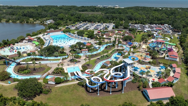 Vista aérea de um parque aquático com vários toboáguas e piscinas, cercado por estacionamento e áreas verdes.