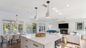 Uma cozinha moderna com uma ilha central, área de jantar com cadeiras, lareira e sala de estar com sofá.