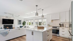 Cozinha moderna com armários brancos, uma ilha central e um espaço de refeições com sofá.