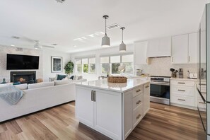 Une cuisine moderne avec des meubles blancs, un îlot central et un coin repas agrémenté d’un canapé.