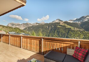 Ein Balkon mit Holzwertlauf, eine gepolsterte Sitzecke mit rotem Karottenkissen und Blick auf die Berge.
