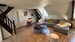 A loft-style living room with a wooden staircase, a gray sofa, a rocking chair, and a coffee table.