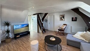 A loft-style living room with a television, a rocking chair, a round ottoman, and a staircase.