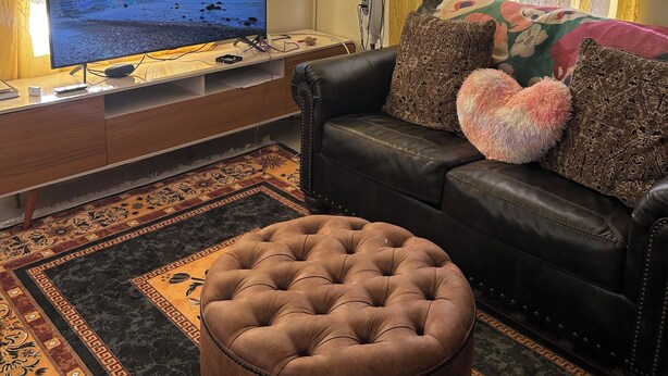 Un soggiorno con televisore, ventilatore, divano e tappeto decorato.