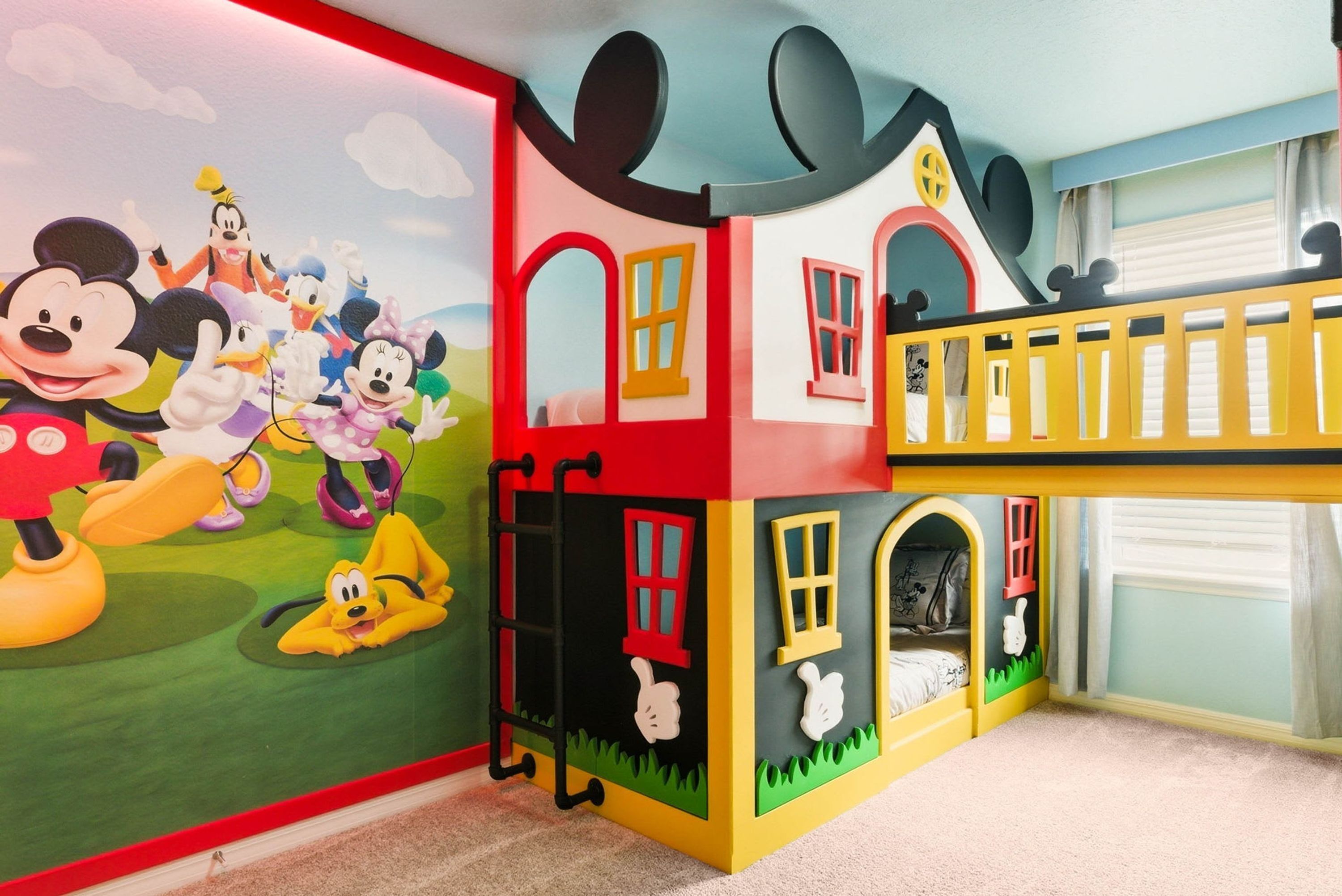 Area giochi per bambini con un murale di personaggi dei cartoni animati, una struttura gioco a più livelli e una finestra con tende.