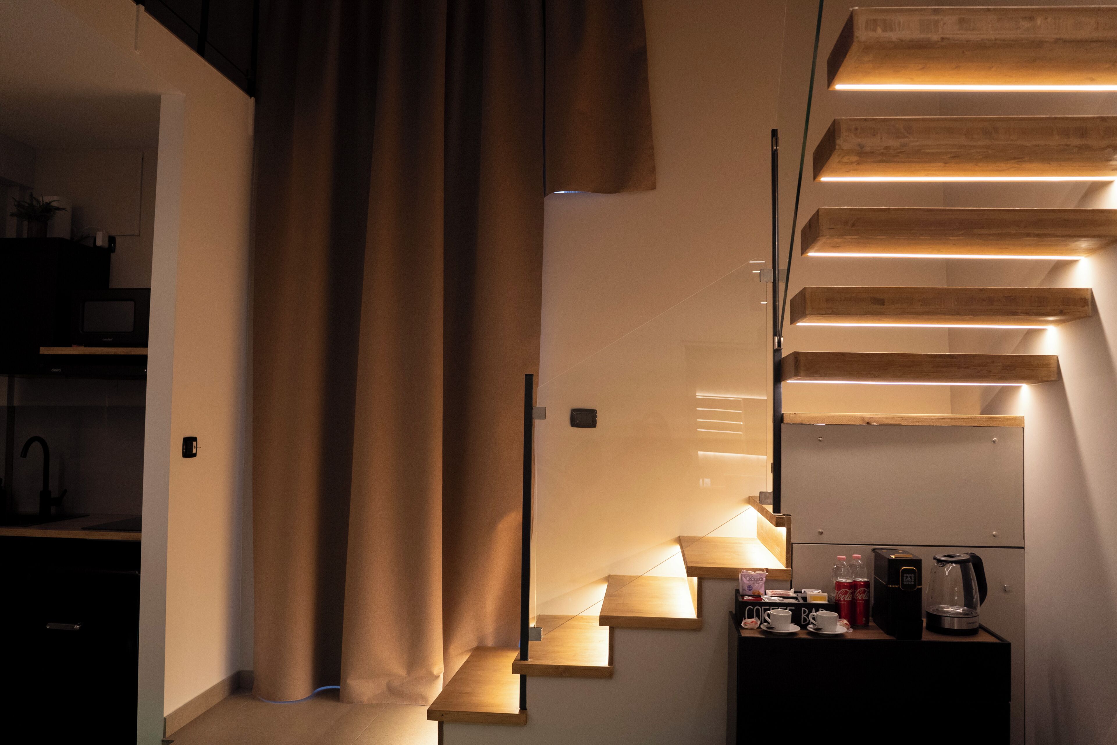 Eine Treppe mit Holzhäusern und integrierter Beleuchtung, die zu einer Zwischenebene mit Kaffeemaschine und kleinem Tisch führt.