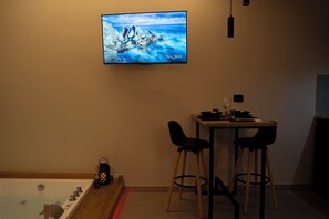 Ein Zimmer mit Badewanne, einem Tisch mit zwei Stühlen, einem an der Wand montierten Fernseher sowie einem kleinen Tisch mit Kerze und Glas.