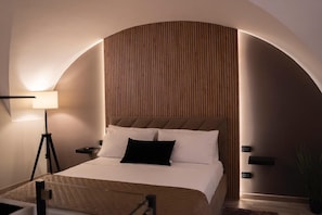 Ein Hotelzimmer mit Bett, Nachttischlampe, Beistelltisch und einer Zimmerpflanze.