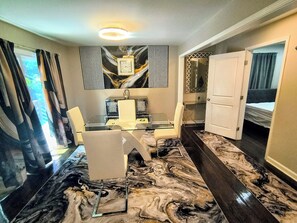 Ein Hotelzimmer mit Glastisch, zwei Stühlen, einem Bett, einer Tür und einem Boden mit Marmoroptik.