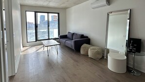 Ein modernes Zimmer mit großem Fenster, einer Couch, einem kleinen Tisch, einem Spiegel und einem runden Hocker.