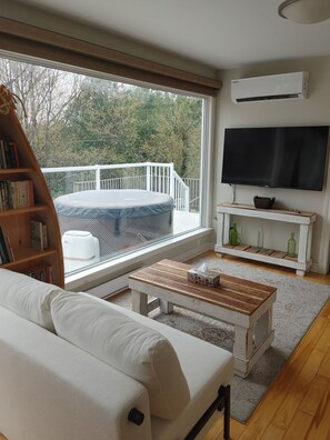 A living room with a sofa, a coffee table, a bookshelf, a TV, and a balcony with a view of trees.
