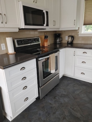 A modern kitchen with white cabinets, a stainless steel stove, a microwave, and a coffee maker.