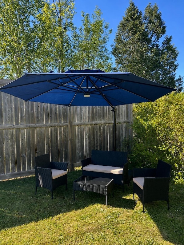 An outdoor patio area with a blue umbrella, wicker furniture, and a wooden fence in the background.