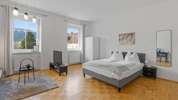 A bedroom with a bed, a chair, a TV, a radiator, and a window with a view.