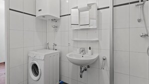 A modern bathroom with a washing machine, sink, and shower. - FarawayHomes Studio Krieglach 14 (Sommer)